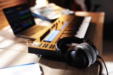 Photo of MIDI keyboard with headphones, laptop and dj mixer on wooden table indoors, closeup
