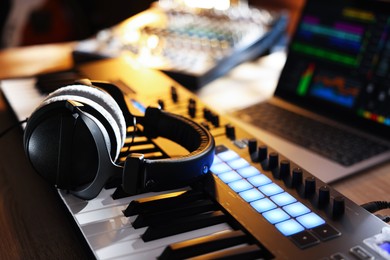 Photo of MIDI keyboard with headphones, laptop and dj mixer on wooden table indoors, closeup