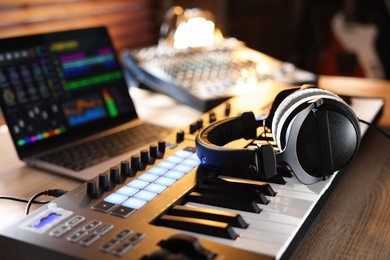 Photo of MIDI keyboard with headphones, laptop and dj mixer on wooden table indoors, closeup