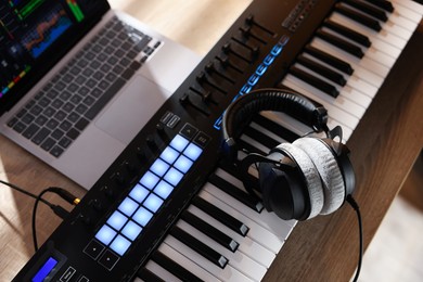 Photo of MIDI keyboard with headphones and laptop on wooden table, above view