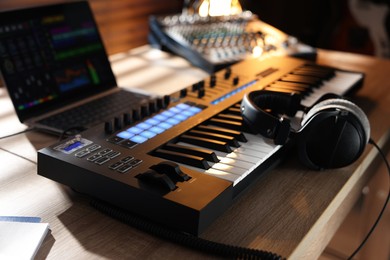 Photo of MIDI keyboard with headphones, laptop and dj mixer on wooden table indoors, closeup