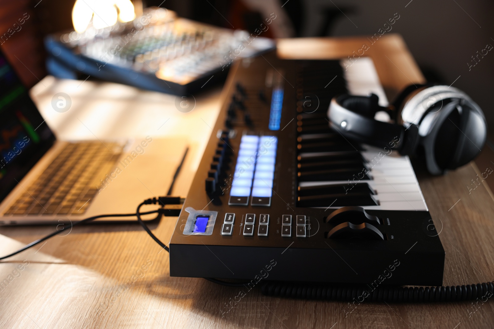 Photo of MIDI keyboard with headphones, laptop and dj mixer on wooden table indoors, closeup