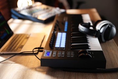 Photo of MIDI keyboard with headphones, laptop and dj mixer on wooden table indoors, closeup