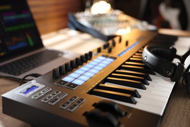 Photo of MIDI keyboard with headphones, laptop and dj mixer on wooden table indoors, closeup
