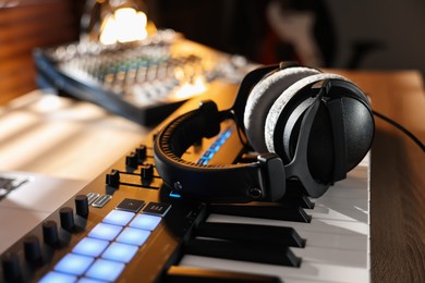 Photo of MIDI keyboard with headphones and dj mixer on table indoors, closeup