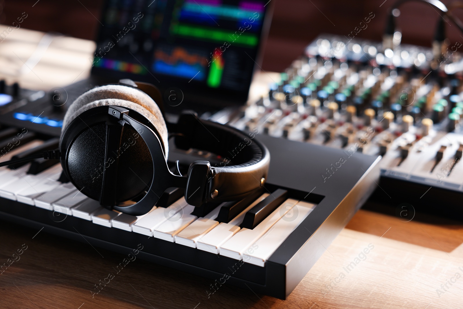 MIDI keyboard with headphones, dj mixer and laptop on wooden table, closeup Photo of MIDI keyboard with headphones, dj mixer and laptop on wooden table, closeup
