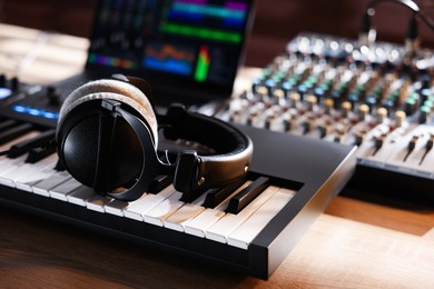 Photo of MIDI keyboard with headphones, dj mixer and laptop on wooden table, closeup