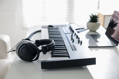 Photo of MIDI keyboard, headphones and laptop on white wooden table indoors, closeup