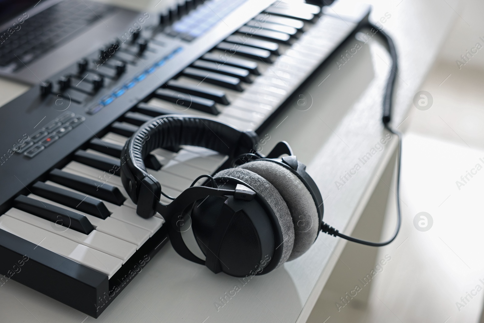 MIDI keyboard with headphones on white wooden table indoors, closeup Photo of MIDI keyboard with headphones on white wooden table indoors, closeup