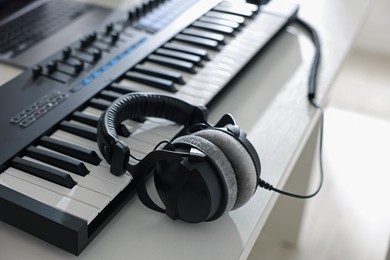 Photo of MIDI keyboard with headphones on white wooden table indoors, closeup