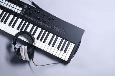 Photo of MIDI keyboard with headphones on grey background, top view. Space for text