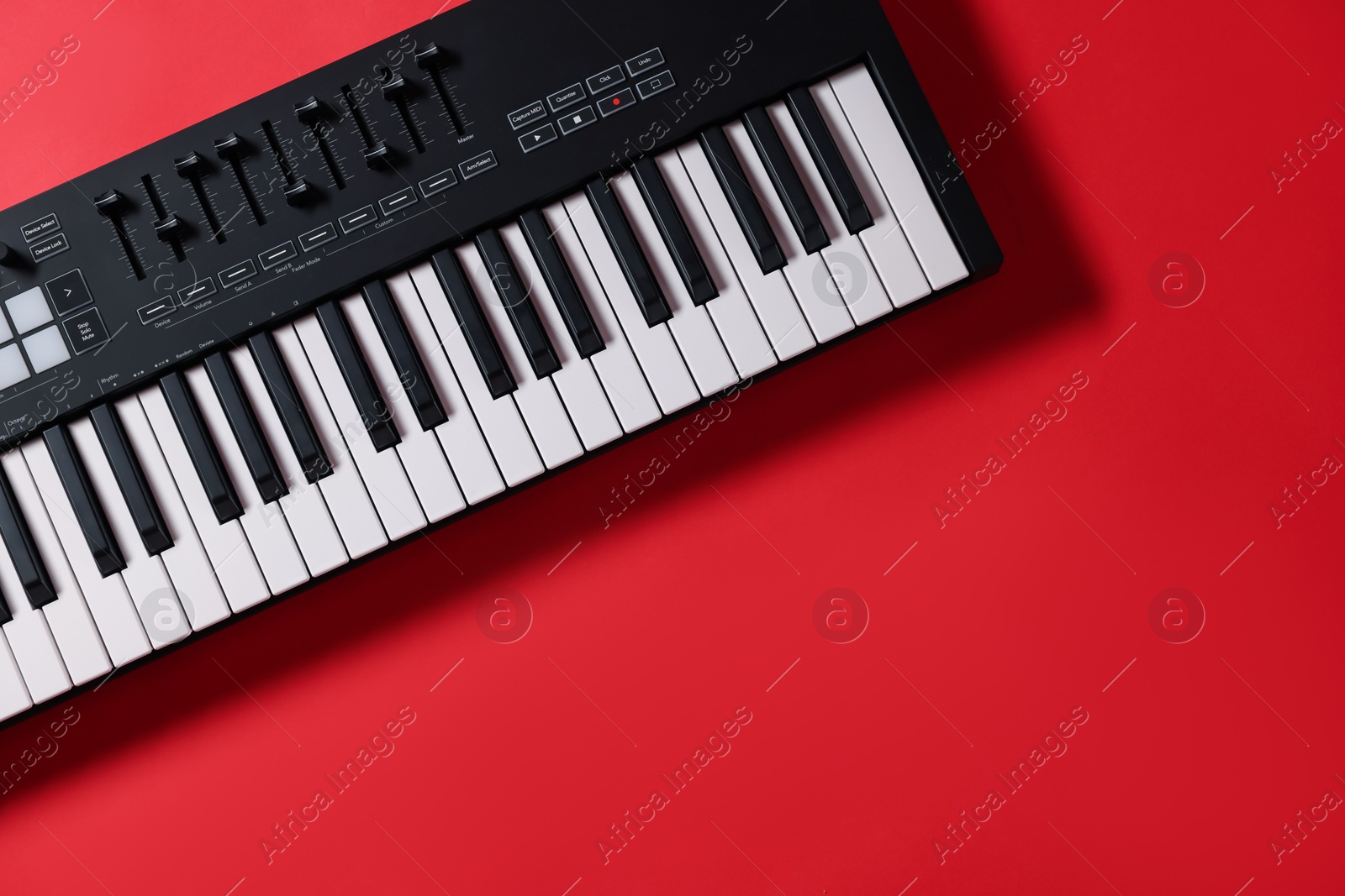 One portable MIDI keyboard on red background, top view. Space for text Photo of One portable MIDI keyboard on red background, top view. Space for text