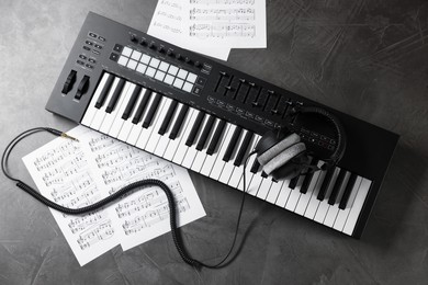Photo of MIDI keyboard, headphones and music sheets on grey table, flat lay