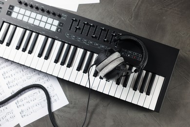 Photo of MIDI keyboard, headphones and music sheets on grey table, flat lay