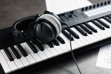 Photo of MIDI keyboard, headphones and music sheets on grey table, closeup