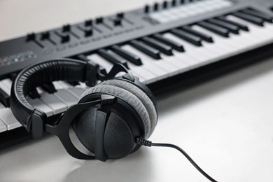 Photo of MIDI keyboard with headphones on white table, closeup