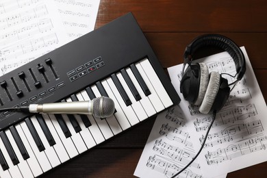 Photo of MIDI keyboard, headphones, microphone and music sheets on wooden table, flat lay