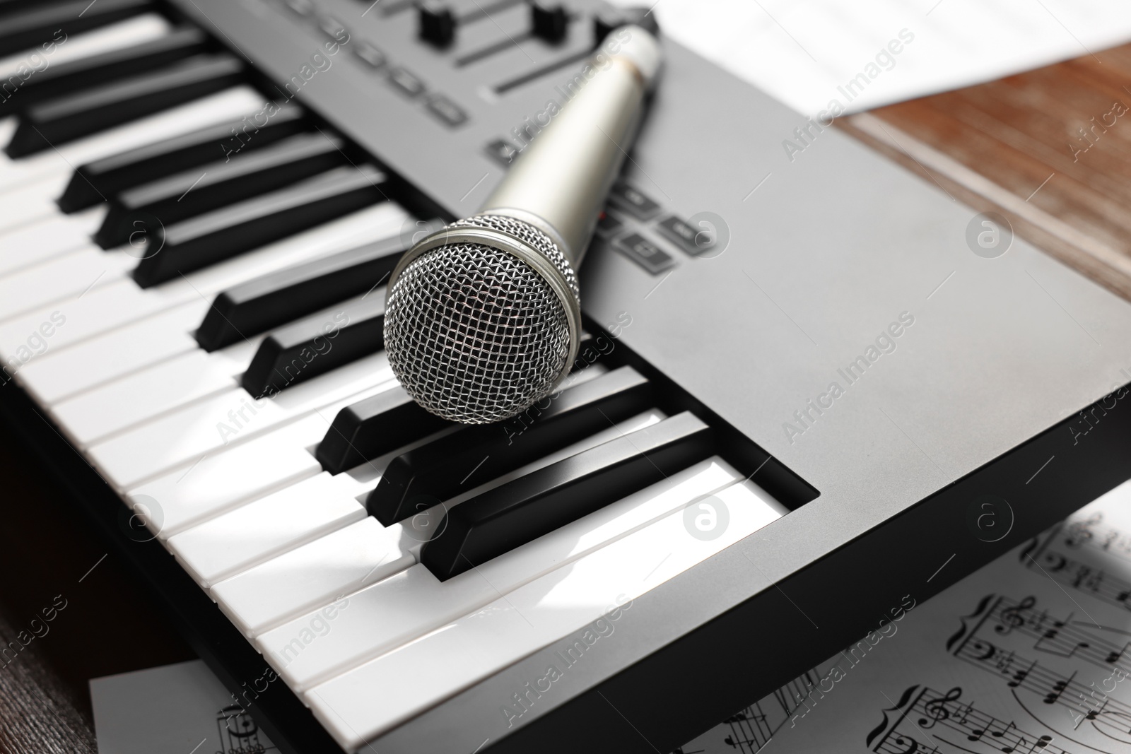 MIDI keyboard, microphone and music sheets on table, closeup Photo of MIDI keyboard, microphone and music sheets on table, closeup