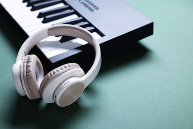 Photo of MIDI keyboard and headphones on green background, closeup. Space for text