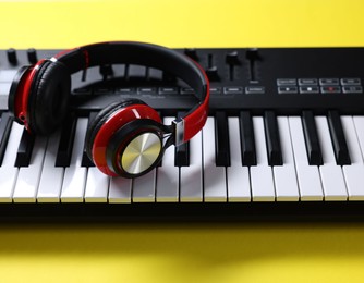 Photo of MIDI keyboard with headphones on yellow background, closeup
