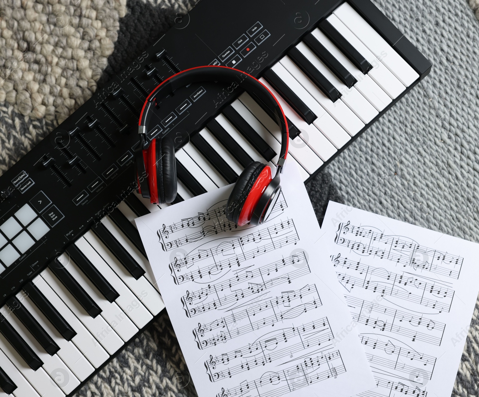 Photo of MIDI keyboard, music sheets and headphones on carpet, flat lay