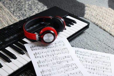 Photo of MIDI keyboard, music sheets and headphones on carpet, closeup