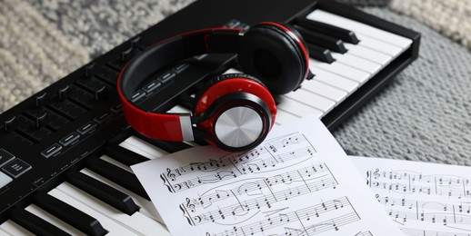 Photo of MIDI keyboard, music sheets and headphones on carpet, closeup
