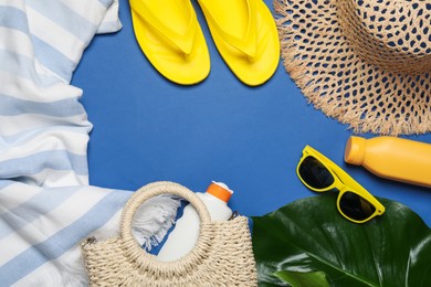 Photo of Frame of beach accessories and palm leaf on blue background, flat lay. Space for text