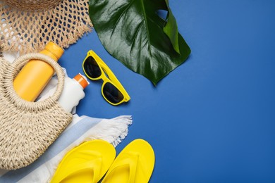 Photo of Beach accessories and palm leaf on blue background, flat lay. Space for text