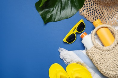 Photo of Beach accessories and palm leaf on blue background, flat lay. Space for text