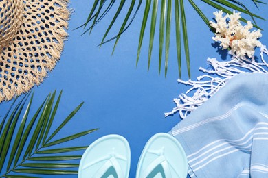 Photo of Frame of beach accessories and palm leaves on blue background, flat lay. Space for text