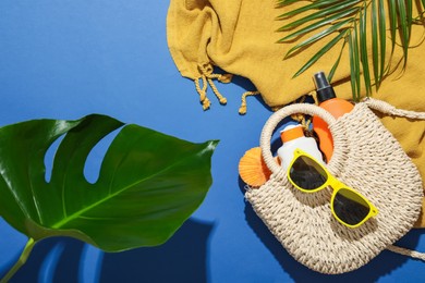 Photo of Beach accessories and palm leaves on blue background, flat lay