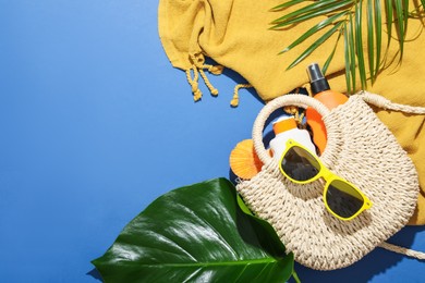 Photo of Beach accessories and palm leaves on blue background, flat lay. Space for text