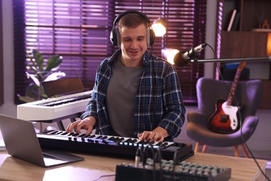 Photo of Smiling man in headphones working with MIDI keyboard at table in home studio