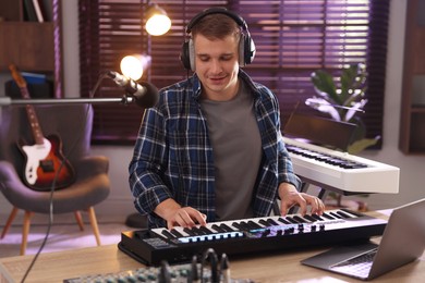 Photo of Man in headphones working with MIDI keyboard at table in home studio