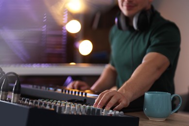 Photo of Man working with MIDI keyboard and dj mixer at table in home studio, selective focus