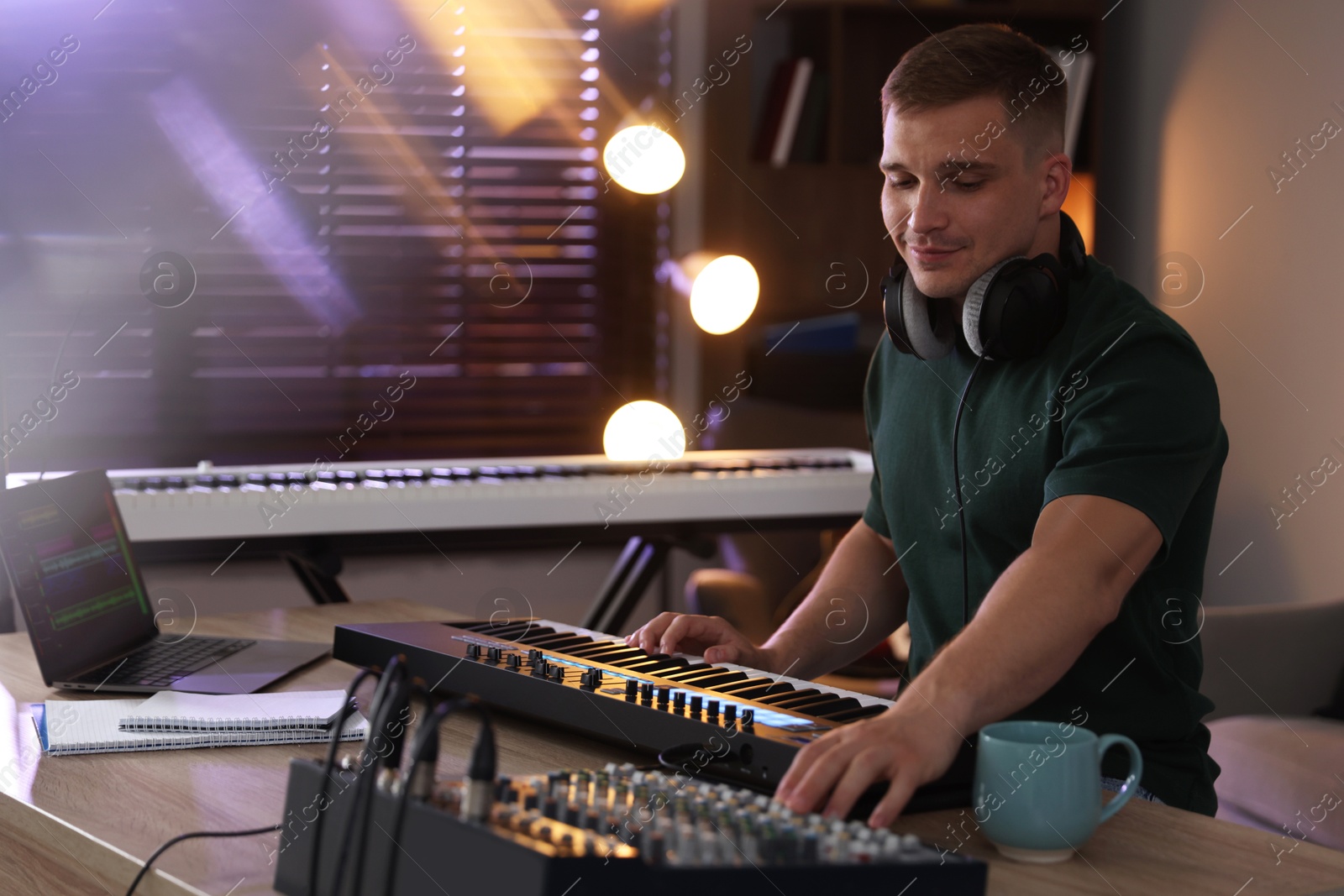 Photo of Man working with MIDI keyboard and dj mixer at table in home studio