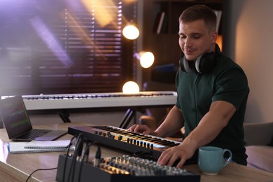 Photo of Man working with MIDI keyboard and dj mixer at table in home studio