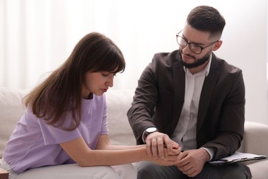 Photo of Psychologist supporting patient during therapy session on sofa in office