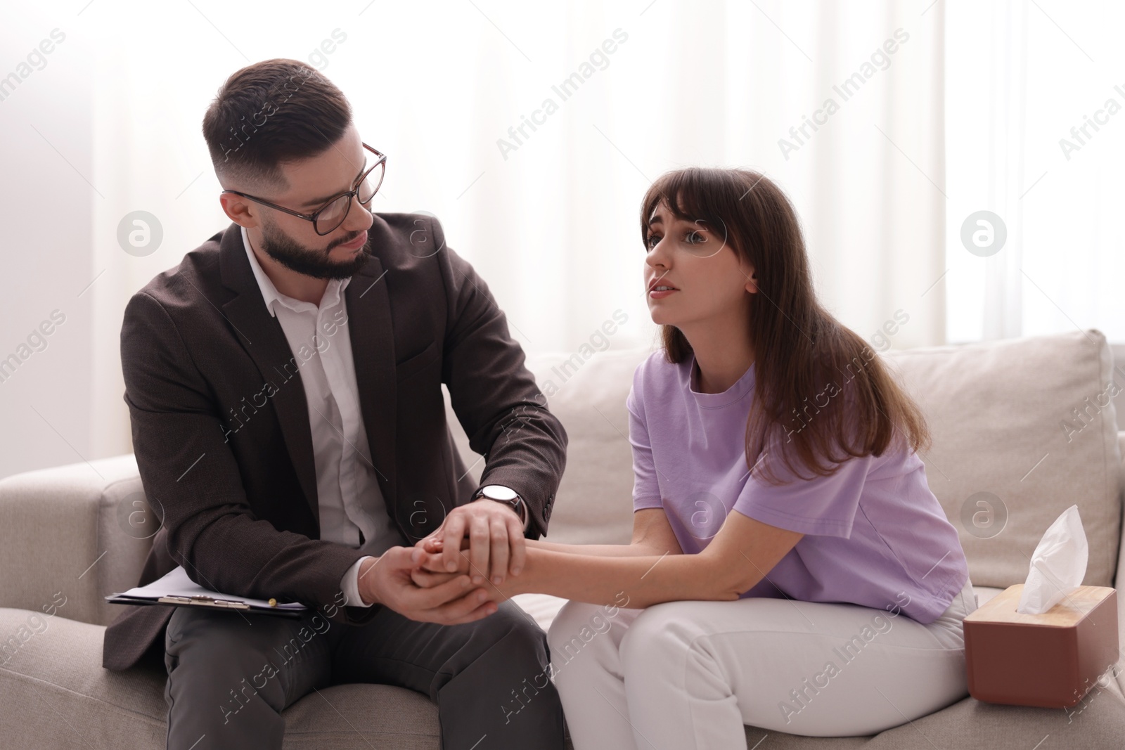 Photo of Psychologist supporting patient during therapy session on sofa in office