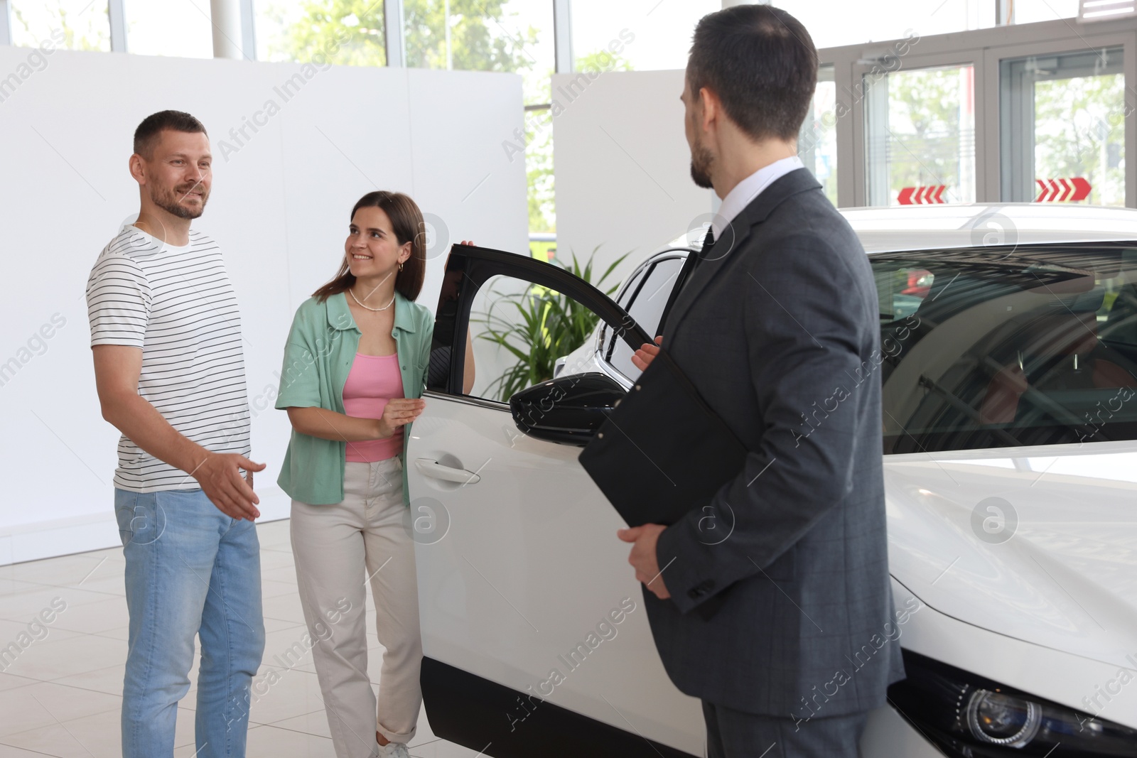 Photo of Salesman with clipboard showing new car to happy family in salon