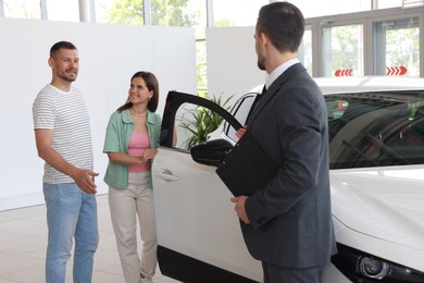 Photo of Salesman with clipboard showing new car to happy family in salon