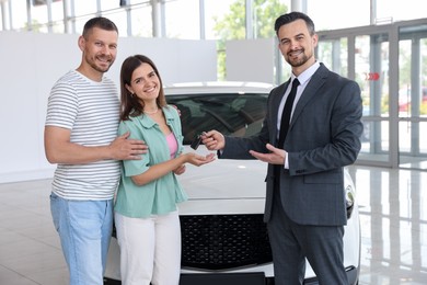 Photo of Smiling salesman giving car key to happy family in salon