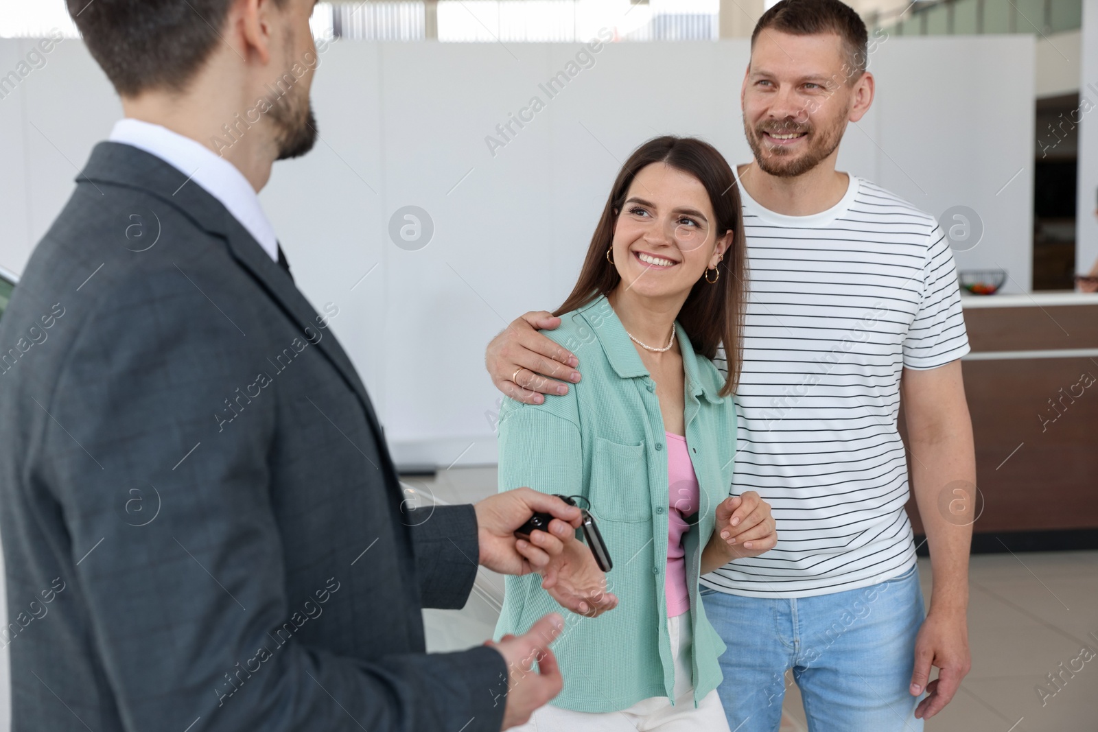 Photo of Salesman giving car key to happy family in salon