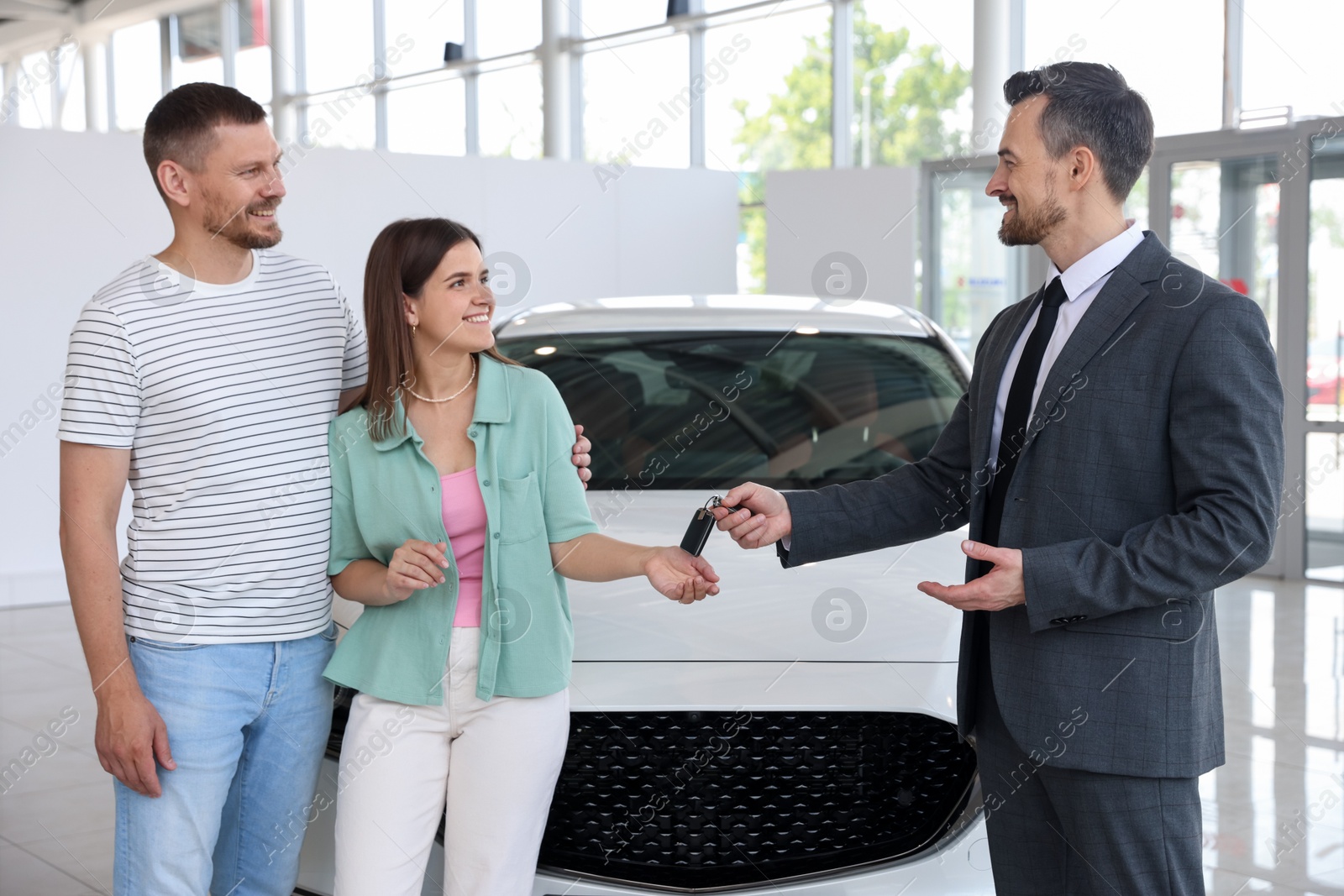 Photo of Smiling salesman giving car key to happy family in salon