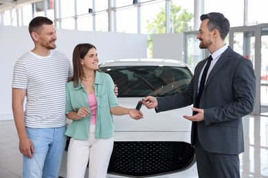 Photo of Smiling salesman giving car key to happy family in salon