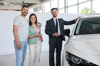 Photo of Happy family, salesman and new car in salon