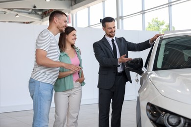 Photo of Salesman showing new car to happy family in salon