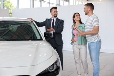 Photo of Salesman showing new car to happy family in salon