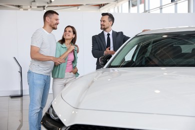 Photo of Salesman showing new car to happy family in salon